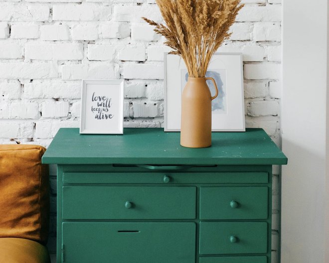 A tidy and neat green drawer with picture frames and a vase on top.